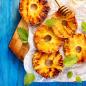 Preview: Gegrillte Ananasscheiben mit Honig beträufelt blauer rustikaler Hintergrund