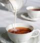 Preview: Weiße Teetassen mit Tee gefüllt werden gerade mit Milch gefüllt weißer Hintergrund