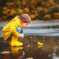 Preview: Kind was an eine Pfützemit einem Papierboot spielt in gelber Regenkleidung rustikaler Hintergrund