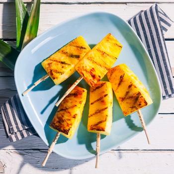 Ananas am Stiel auf einem hellblauen Teller im Hintergrund