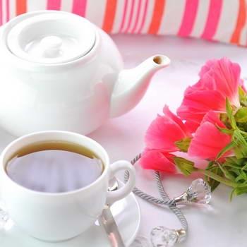 Weiße Teetasse und weiße Teekanne mit rosa Blumen auf weißer Tischdecke im Hintergrund