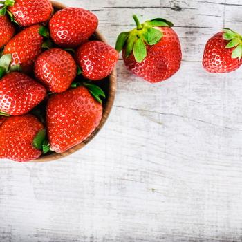 Erdbeeren in einer Schale und 2 Erdbeeren davor heller rustikaler Hintergrund