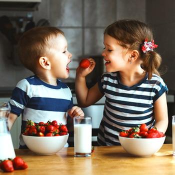 Zwei Kinder die Erdbeeren naschen das Mädchen füttert ihren kleinen Bruder rustikale Küche im Hintergrund