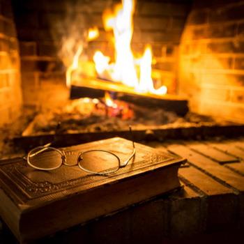 Buch und Brille im Vordergrund und Kamin mit Feuer im Hintergrund