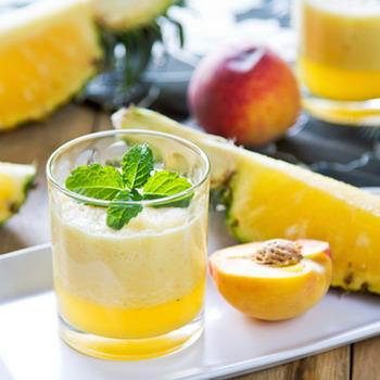 Ananas und Pfirsich aufgeschnitten und ein Glas Fruchtsaft mit Minze heller rustikaler Hintergrund