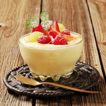 Vanille Pudding mit Himbeeren Trauben und Erdbeeren dekoriert rustikaler Hintergrund