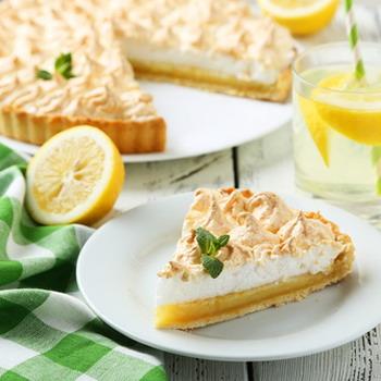 Zitronenkuchen und ein Kuchenstück auf ein Tisch mit einer Zitrone und Glas mit Zitronenschale grüne Tischdecke auf rustikalen Hintergrund