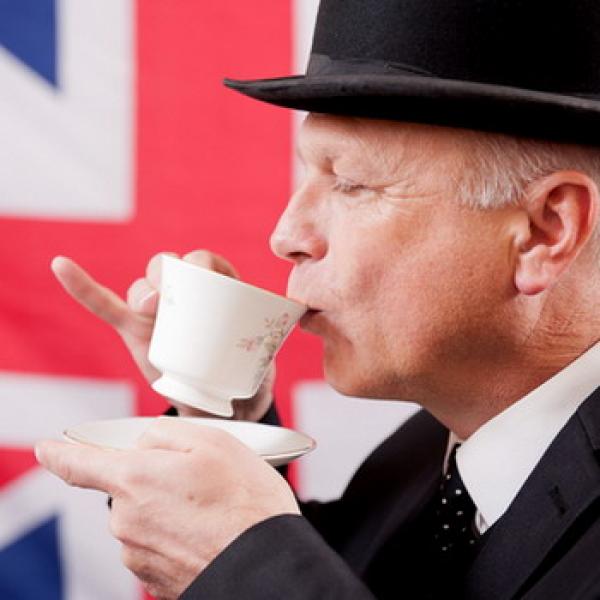 Ein Engländer mit Melone der eine Tasse Tee trinkt vor der Flagge Union Jack im Hintergrund