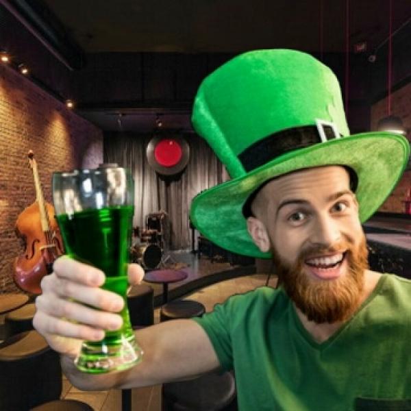 Ein Ire mit grünem Hut und Shirt  mit ein Glas in der Hand steht im Pub Musikinsturmente Hintergrund