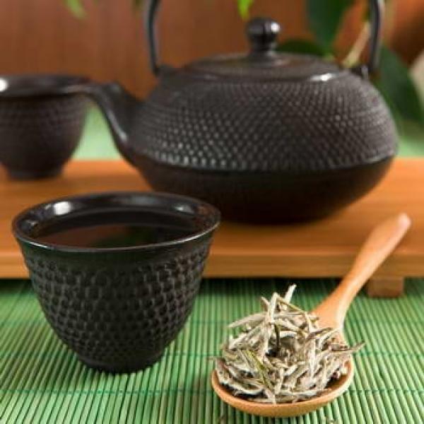 Weißer Tee auf einem Holzlöffel und Gusseiserne Kanne und Becher rustikaler Hintergrund