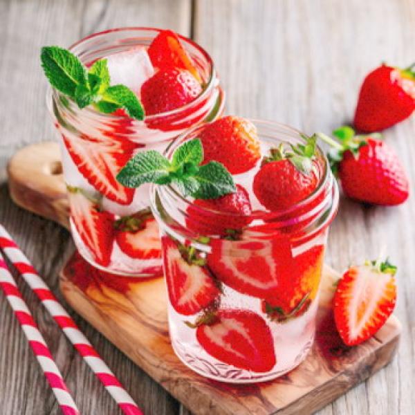 Frischer Erdbeeren im einem Glas mit Wasser und 2 Strohalme daneben rustikaler Hintergrund