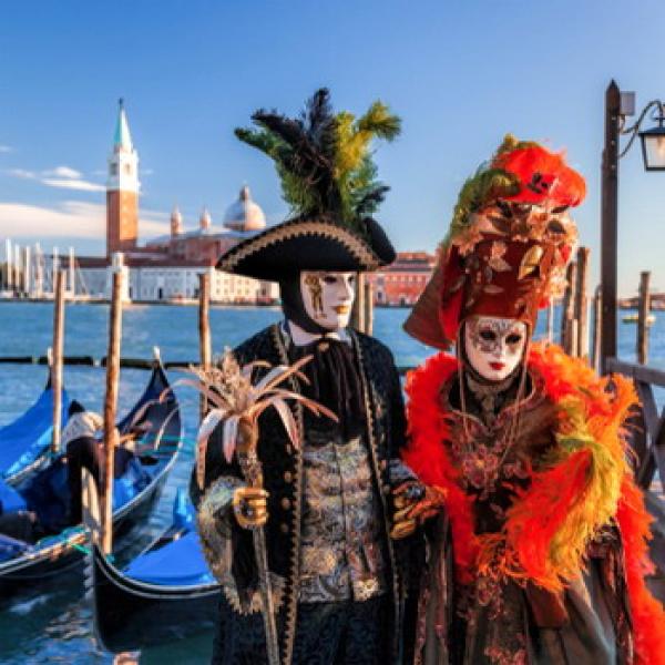 Mann und Frau mit venezianischen Kostüm in Venedig mit Booten im Hintergrund