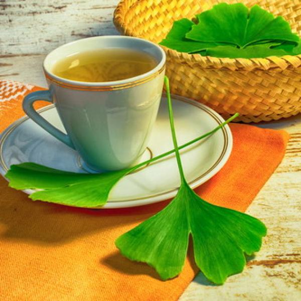Teetasse mit Tee und Ginkgoblätterdavor und dahinter im Korb heller rustikaler Hintergrund Hintergrund
