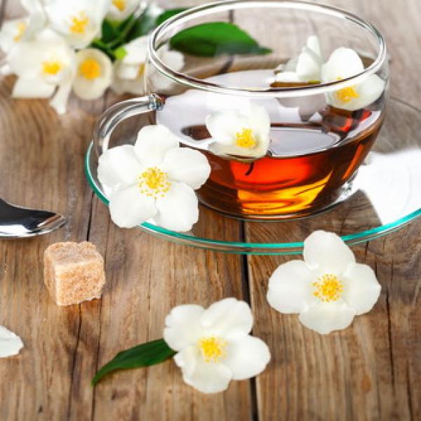 Jasminblüten mit einer Tasse grünen Glas Tee mit Rohrzucker Würfel auf rustikalen Hintergrund