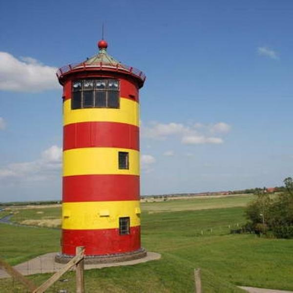 Rot gelber gestreifter Leuchtturm auf einer Wiese im Vordrgrund und strahlender blauer Himmel im Hintergrund