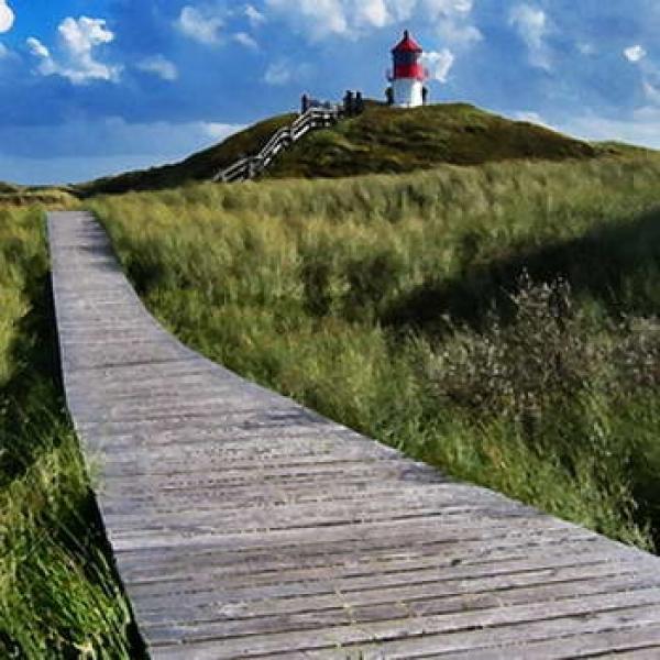 Friesischer Landschaft mit Holzsteg durch die Dünen mit Leuchturm im Hintergrund