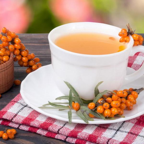 Tasse mit Tee und Sanddornbeeren daneben mit kleiner Tischdecke rustikaler Hintergrund