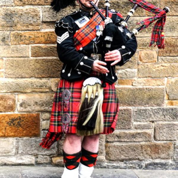 Ein Schotte der Dudelsack spielt sein Kopf und Füße sind nicht zu sehen rustikale Steinmauer als Hintergrund
