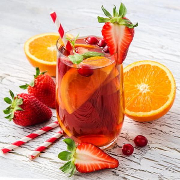 Glas mit frischen halben Orangen und leckeren Erdbeeren darin und davor rustikaler Hintergrund